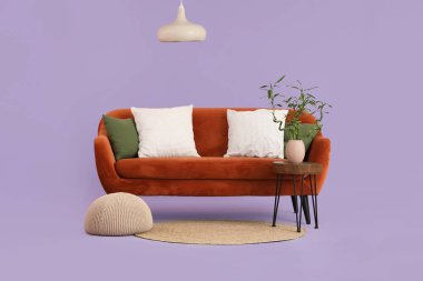 Vazoda bambu saplı masa, kırmızı kanepe, eflatun arkaplanda puf ve lamba.