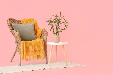 Vazoda bambu saplı masa, pembe arka planda hasır koltuk ve halı.