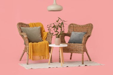 Vazoda bambu saplı masa, pembe arka planda koltuklar ve lamba.
