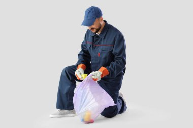 Male scavenger throwing garbage into bag on light background clipart