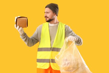 Male scavenger with food container and garbage bag on yellow background clipart