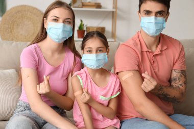 Aşıdan sonra maskeli bir aile evdeki kanepede kalp jesti yapıyor.
