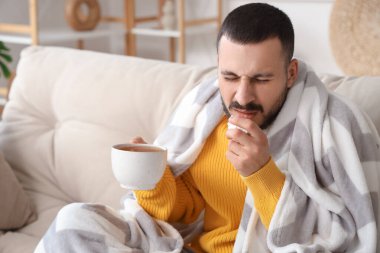 Evdeki kanepede hapşıran limonlu çaylı genç adam.