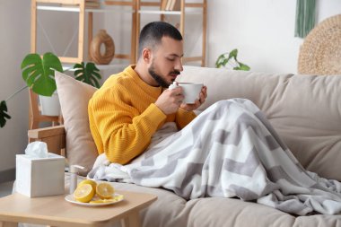 Evdeki kanepede limon çayı içen genç adam.