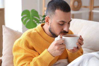 Evdeki kanepede limon çayı içen genç adam.