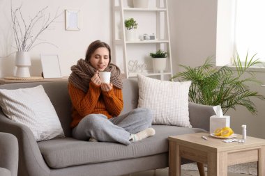 Evde kanepede oturan limonlu çaylı genç bir kadın.