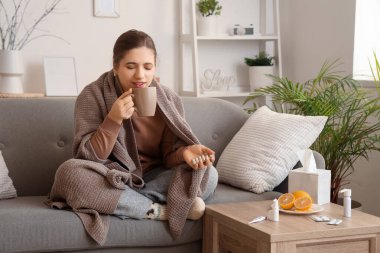 Evdeki kanepede limon çayı içen haplı genç bir kadın.