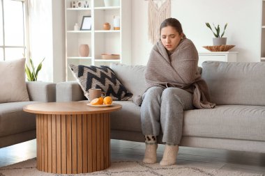 Evdeki masada ekose ve limonlu çay içen hasta genç bir kadın.