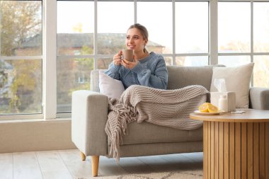 Evdeki kanepede limon çayı içen genç bir kadın.