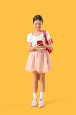 Sırt çantalı genç kız sarı arka planda cep telefonu kullanıyor.