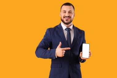 Sarı arka planda cep telefonuna işaret eden kravatlı genç bir işadamı