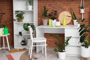 Atölyedeki tuğla duvarın yanında raf ünitesi, bitki ve bahçe aletleri olan çalışma yeri