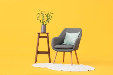 Vazoda bambu saplı masa, sarı arka planda koltuk ve halı.