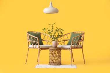 Vazoda bambu saplı masa, sarı arka planda koltuklar ve lamba.