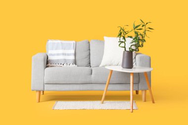 Vazoda bambu saplı masa, gri kanepe ve sarı arka planda halı.