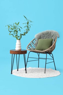 Vazoda bambu saplı masa, mavi arka planda koltuk ve halı.
