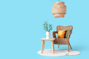 Vazoda bambu saplı masa, mavi arka planda hasır koltuk, halı ve lamba.