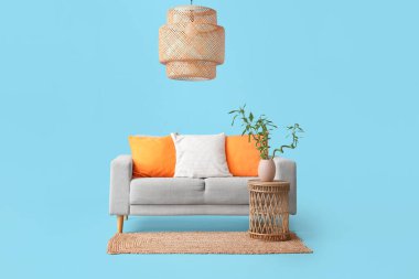 Vazoda bambu saplı masa, gri kanepe, mavi arka planda halı ve lamba.