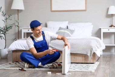 Tornavidalı erkek teknisyen yatak odasındaki elektrikli konteyner ısıtıcısını tamir ediyor.