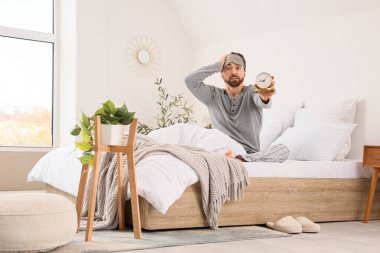 Stresli bir sabah, çalar saati olan genç adam yatak odasında oturuyor.