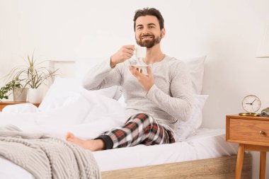 Yatak odasında kahve fincanı olan yakışıklı bir adamın sabahı.