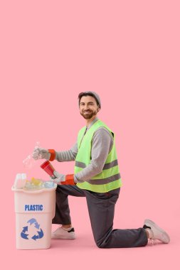 Erkek çöpçü, pembe arka plandaki çöp kutusuna plastik çöp atıyor.