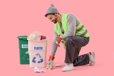 Pembe arka planda çöp ve çöp bidonları olan erkek çöpçü.