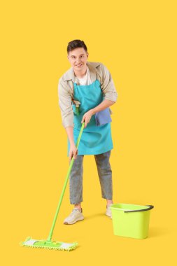 Önlüklü genç adam sarı arka planı paspaslıyor.