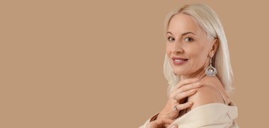 Bej arka planda güzel mücevherler takan modaya uygun olgun bir kadın.