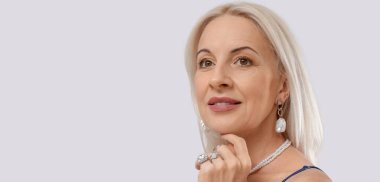 Modaya uygun olgun bir kadın, açık arkaplan üzerine güzel mücevherler takıyor ve mesaj için yeri var.