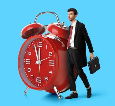 Genç iş adamı ve açık mavi arka planda büyük bir çalar saat. Zaman yönetimi kavramı