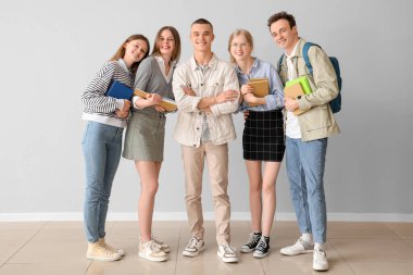 Gri duvarın yanında kitapları olan bir grup öğrenci.