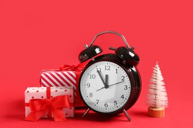 Kırmızı arka planda Noel kutlaması için köknar ağacı ve hediye kutulu çalar saat