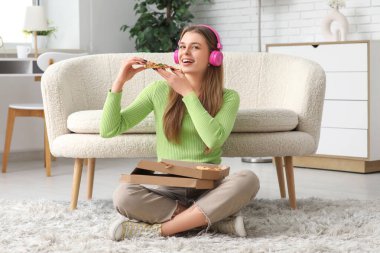 Genç kız oturma odasında lezzetli pizzalar yiyor.