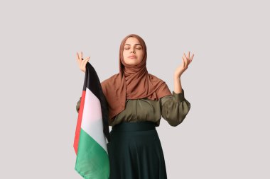 Filistin bayrağı taşıyan genç Müslüman kadın gri arka planda dua ediyor. Üzüntü konsepti