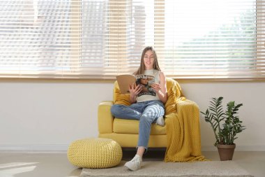 Yastık ve ekoseli koltukta oturmuş dergi okuyan genç bir kadın.