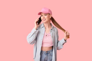 Pembe arka planda cep telefonuyla konuşan şık şapkalı güzel bir genç kadın.