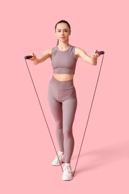 Pembe arka planda ip atlayan genç bir bayan antrenör.