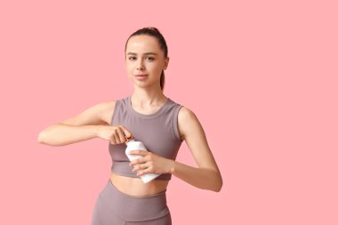 Pembe arka planda bir şişe su ve havlusu olan genç bir kadın.