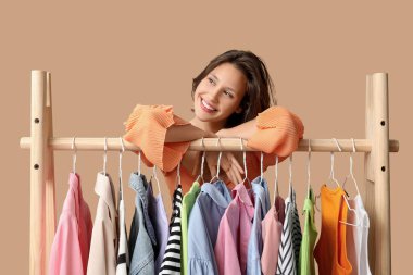 Bej arka planda farklı giysileri olan rafların yanında güzel genç bir kadın.