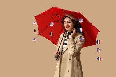 Young happy African-American woman holding umbrella with USA and France flags on beige background clipart