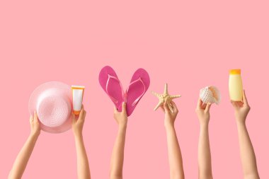 Plaj aksesuarları ve pembe arka planda parmak arası terlikleri olan kadın elleri.