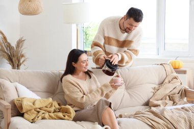 Mutlu genç adam sonbahar günü evinde karısına çaydanlıktan çay dolduruyor.