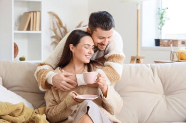 Sonbahar günü evde çay içip kucaklaşan mutlu genç çift.