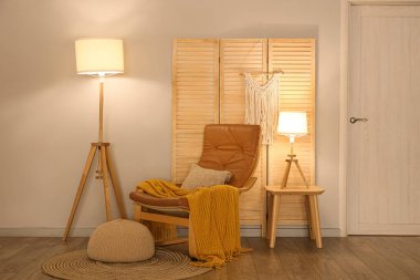 Koltuk, puf, katlanan ekran ve oturma odasının içinde parlayan lambalar.