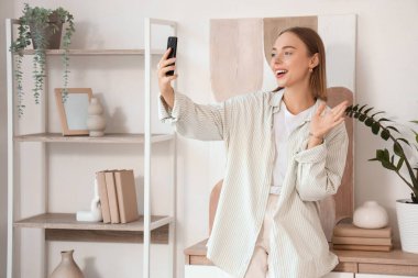 Cep telefonlu genç bir kadın evde görüntülü sohbet ediyor.