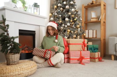 Noel Baba şapkalı genç kadın Noel arifesinde şöminenin yanında oturuyor.