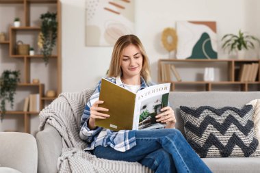 Evdeki kanepede dergi okuyan genç bir kadın.