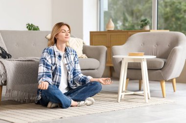 Evde halıda meditasyon yapan genç bir kadın.