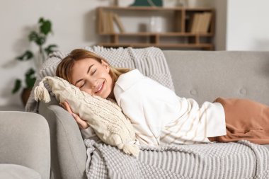 Evdeki gri koltukta yastıklı genç bir kadın dinleniyor.